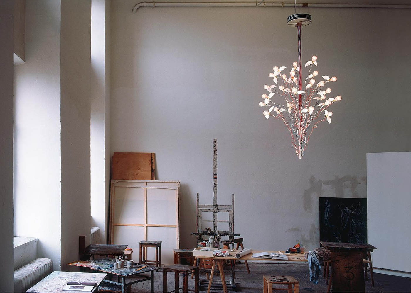 Birds Birds Birds Kronleuchter von Ingo Maurer leuchtet in einem Künstleratelier mit Staffelei, Hockern und Malutensilien
